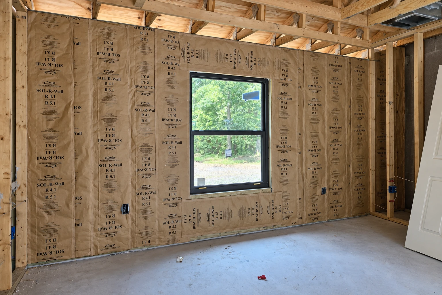 Paper-faced insulation fills the walls of a wood-framed room around a central window.