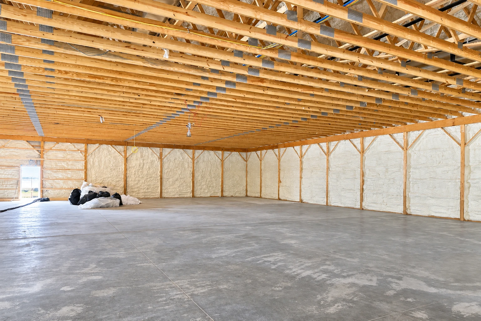 Large commercial building interior with exposed wooden roof trusses and foam insulation covering the walls.
