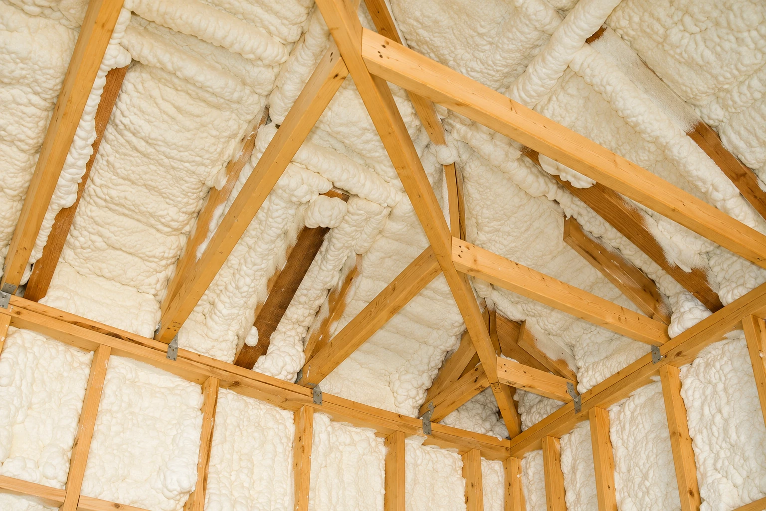 White spray foam insulation fills the spaces between exposed wooden roof trusses.